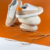 Beige with white shoe being showcased with a branch for decoration and has an orange background