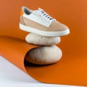 Beige with white shoe being showcased with two rocks underneath for decoration and has an orange background