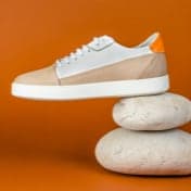 Beige with white shoe being showcased with two rocks underneath for decoration, with the outer side of the shoe being completely shown to user and has an orange background